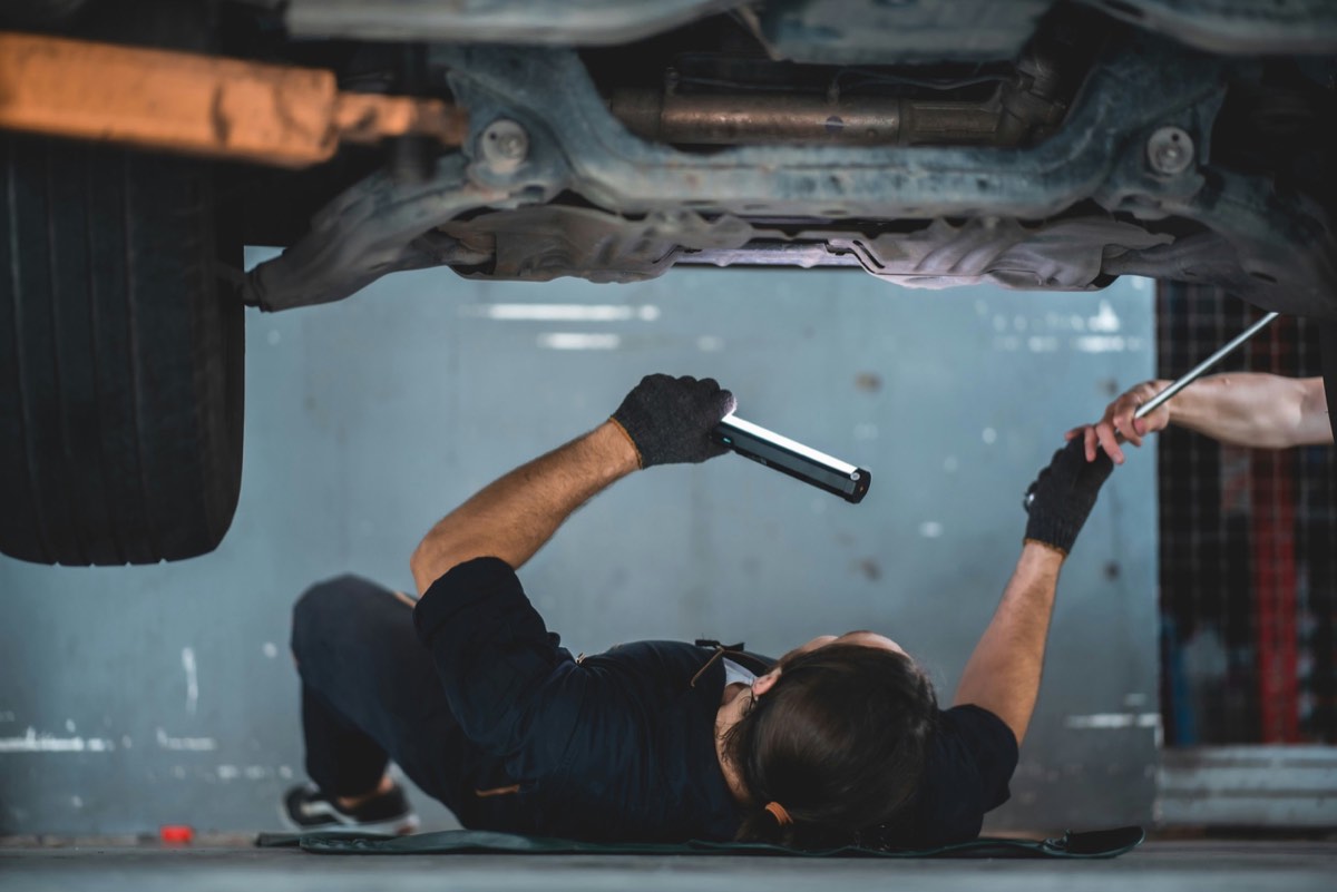 A mechanic working underneath a vehicle with a flashlight in an automotive repair shop.